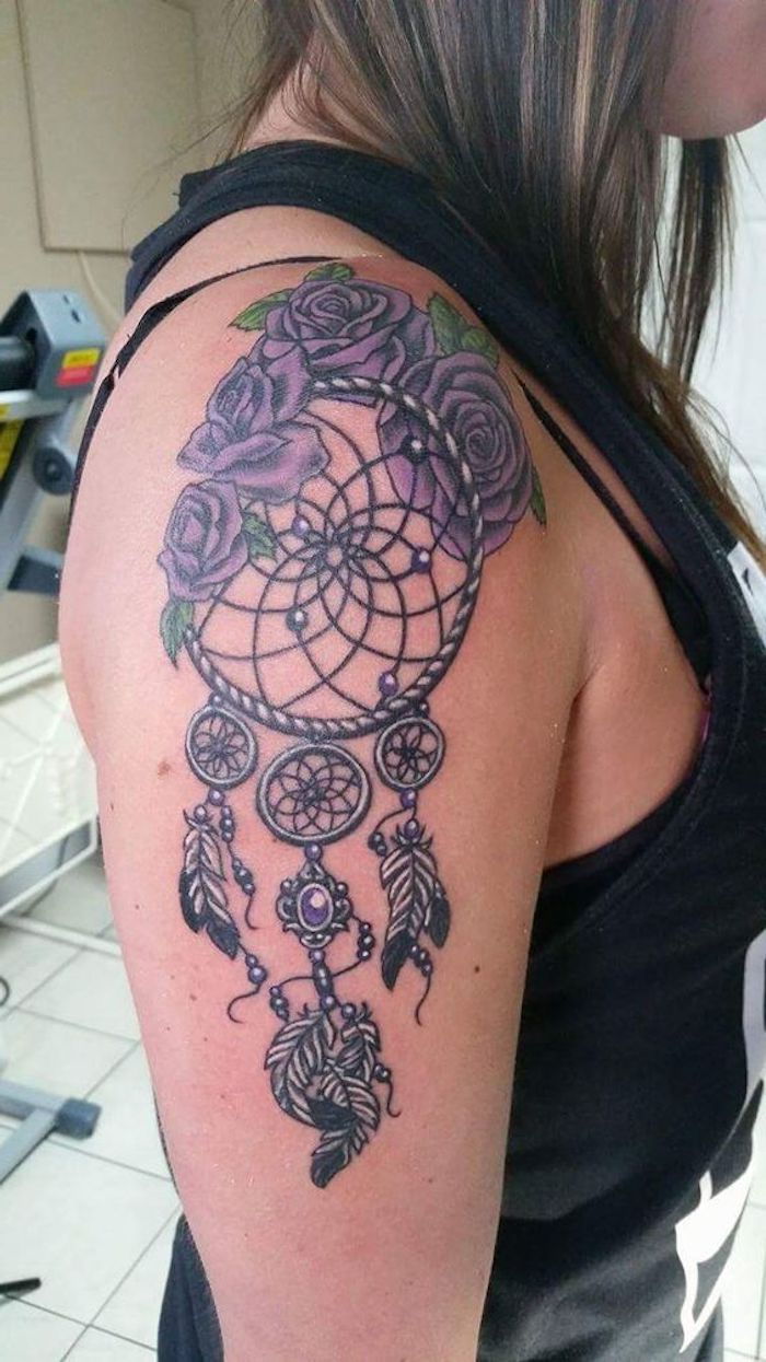 En ide for en tatovering på skulderen til en kvinne med lilla store roser og en drømfanger med fjær
