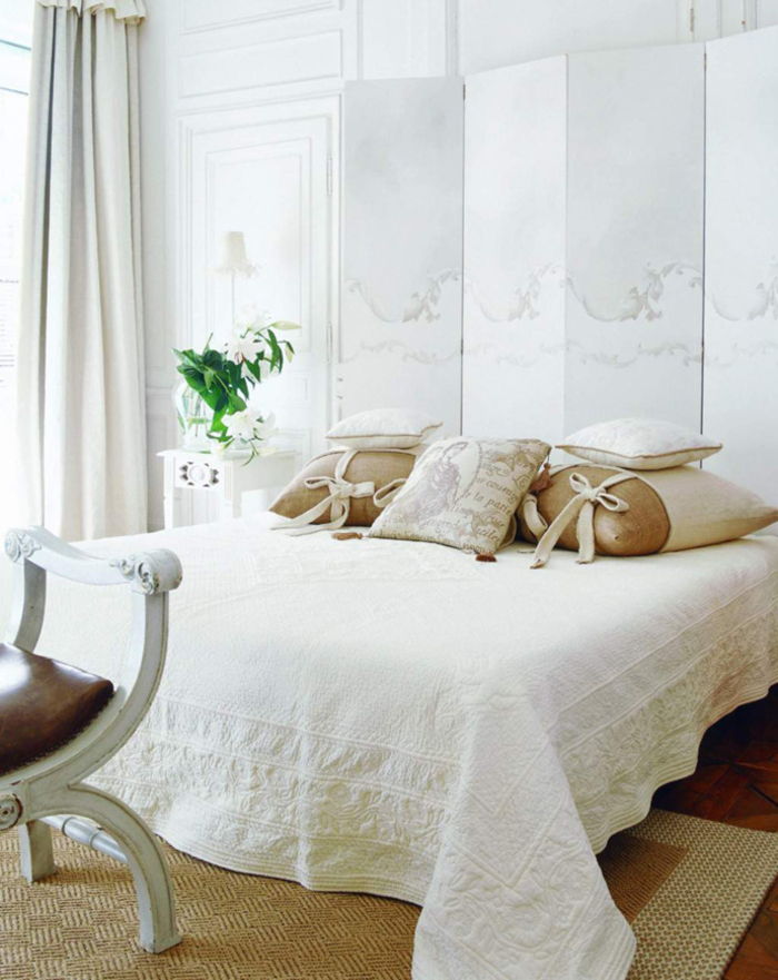 Vintage miegamasis baltos spalvos, daugybė dekoratyvinių pagalvių, vazos gėlės, naktiniai lempos