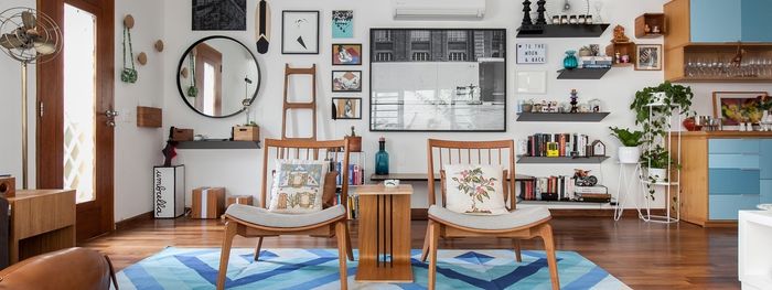 Vintage baldai, medinės kėdės, daug lentynų, kambariniai augalai, paveikslai, mėlynas kilimas ir mėlynos spintelės