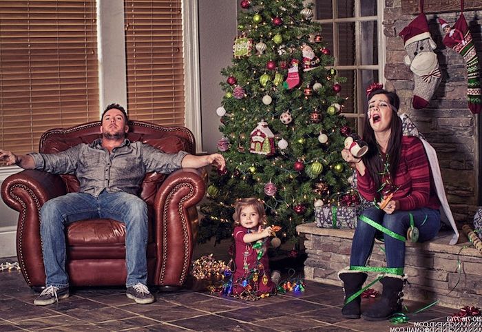 en rolig familj runt julgran, fadern ser utmattad ut, moderen är insvept i ett presentband, bara den lilla prinsessan är glad - julfoton