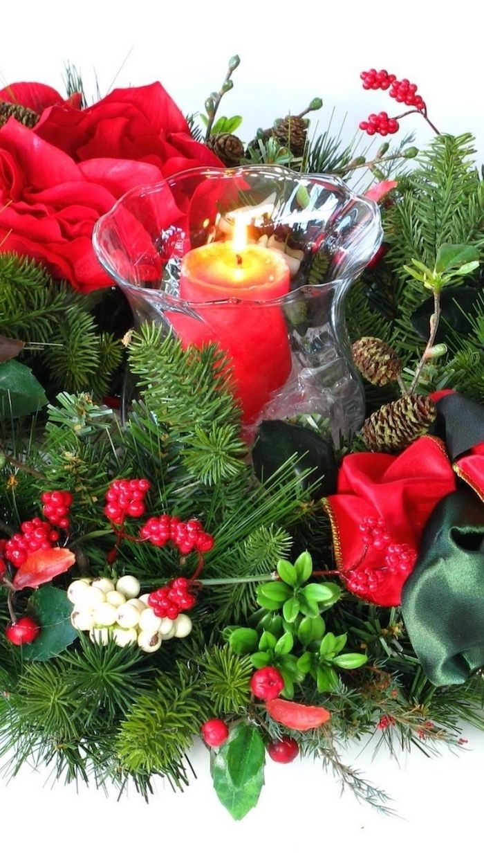sveča v središču rdečih cvetov in zelenih vej - božična ureditev