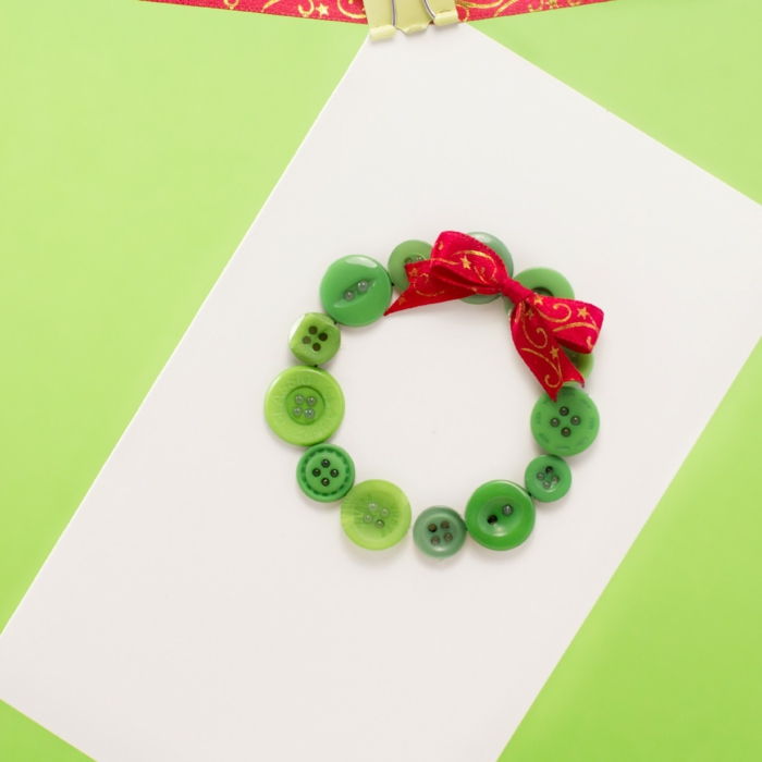Padaryti kalėdines atvirukas, Kalėdų vainikas iš mažų žaliųjų mygtukų ir raudonos dekoratyvinės juostelės