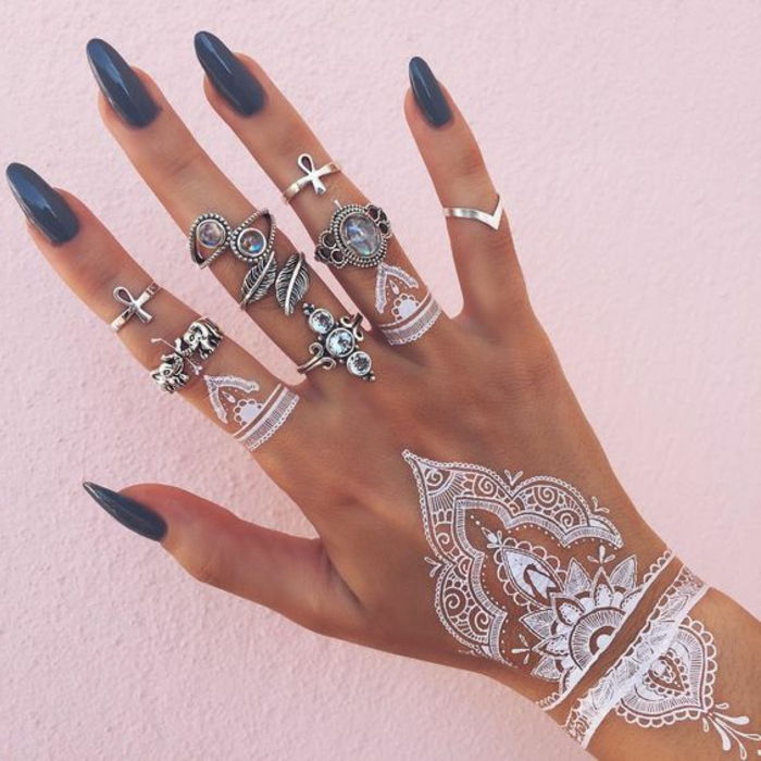 una mano con molti anelli d'argento, tatuaggi con dita bianche, tatuaggio con superficie a mano di henné bianco