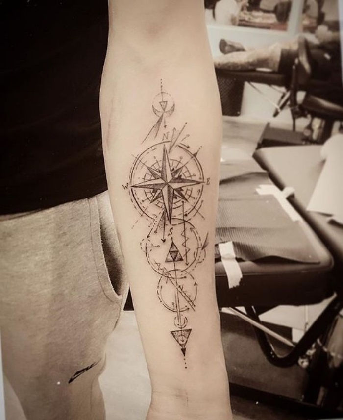To pomysł na tatuaż kompasowy z czarnym kompasem z długimi dużymi czarnymi strzałami
