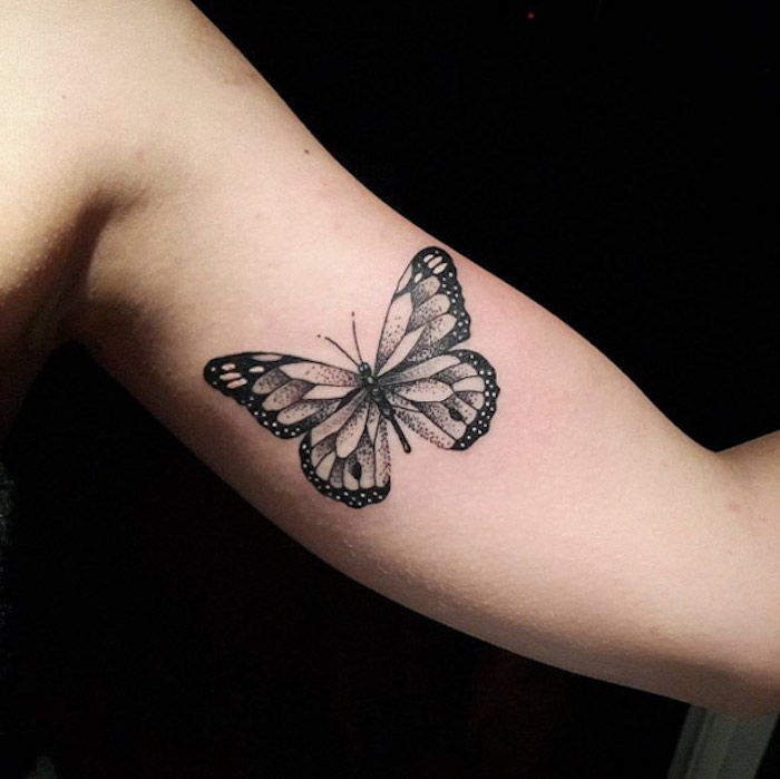 ruka s čiernym tetovacím motýľom - tu je lietajúci čierny motýľ s veľkými čiernymi krídlami