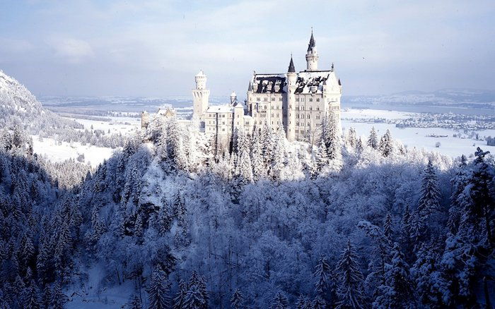 Vinterbilde med et stort hvitt slott med tårn og en skog med mange trær med snø - en himmel med hvite skyer