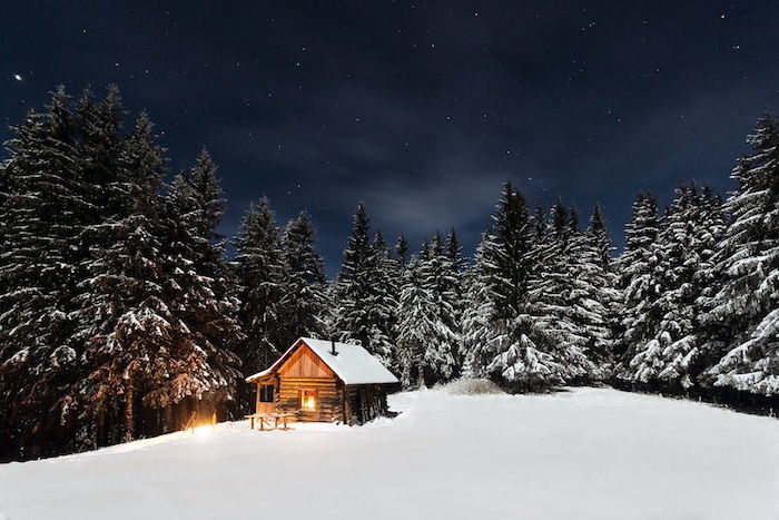 o casă mică de lemn și o pădure cu mulți copaci și zăpadă - un cer cu stele și nori albi