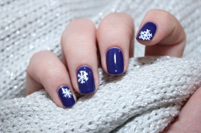 Fulgi de zăpadă alb pe un sol albastru închis, o formă de unghii ovale, idee frumoasă pentru unghiile de iarna pentru re-styling