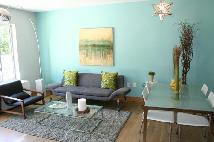 färgsättning vardagsrum matta glasbord Ljus-trägolv och grågrön soffa-kuddar-anläggning automotive-canvas-standardlampa-ljusblå väggar-svart-läder stol