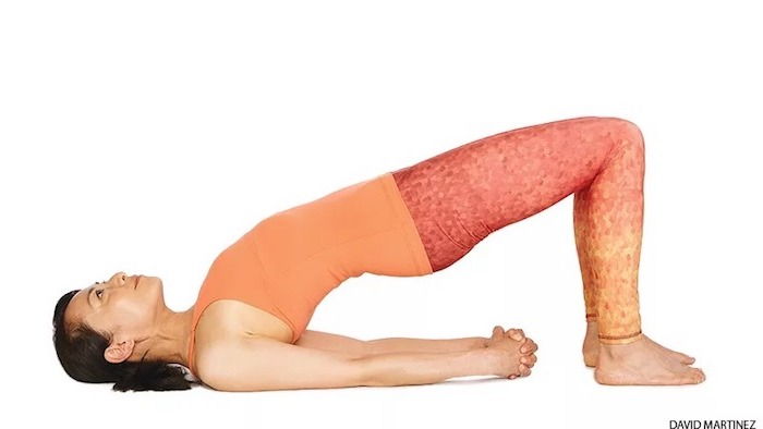 Yoga voor beginners: Aziatische vrouw die de brugpositie uitoefent, uitgestrekte armen en gesloten handen, voeten op de grond, rug en kont in de lucht