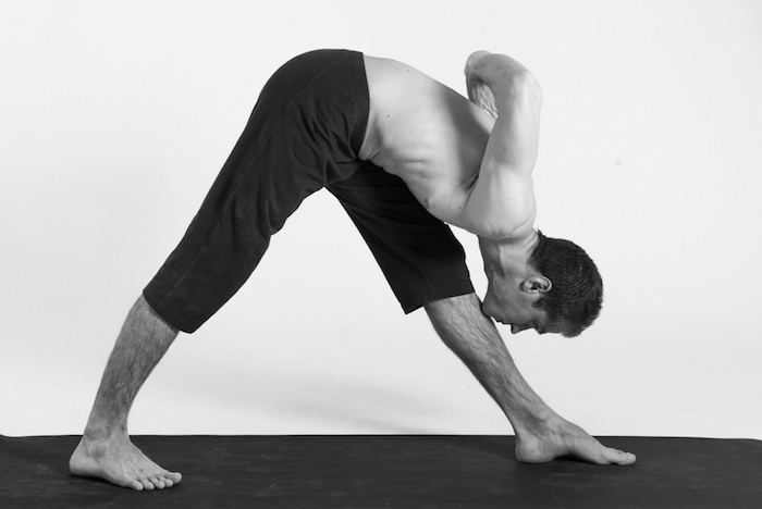 en man som gör yoga, rör på benet med hakan, lutar framåt, svartvitt foto