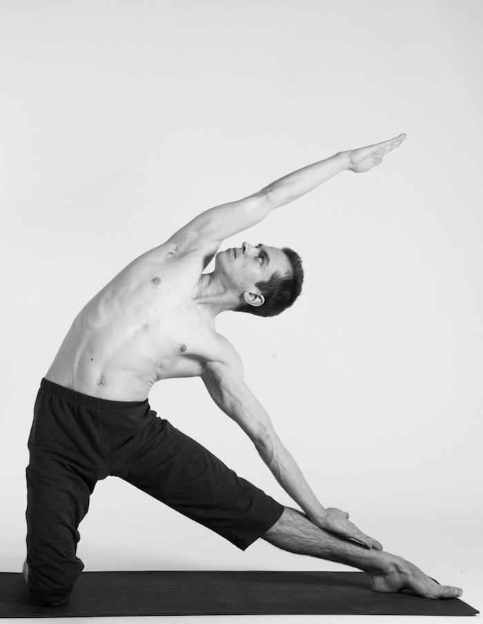 Parighasana yoga posisjon, mann med venstre ben utstrakt og ser opp, svarte sportsbukser til kne