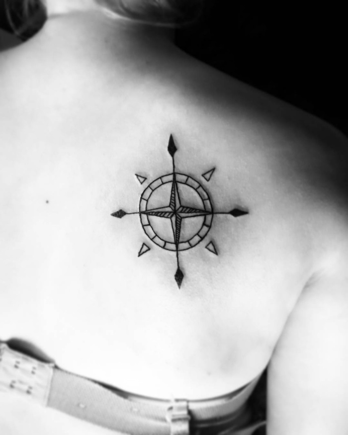 pomysł na czarny tatuaż kompasu na łopatce - tu jest czarny kompas z małymi czarnymi strzałami na grzbiecie młodej kobiety