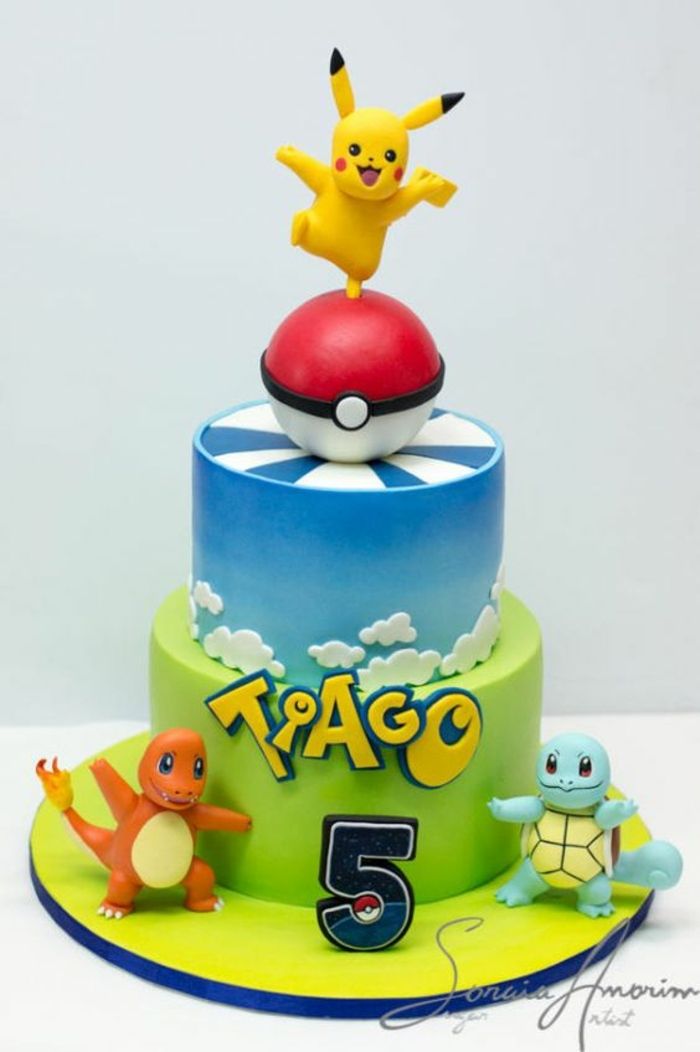 Uma ideia para uma torta de dois andares com uma pokebola vermelha, nuvens, manchetes amarelas, três pequenos seres de pokemon e pikachu